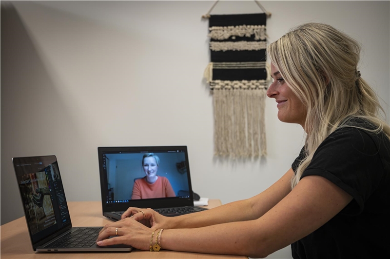 Das Foto zeigt eine junge Frau vor dem Bildschirm und auf einem Laptop daneben.