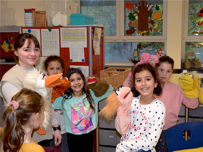 Eine junge Frau steht mit mehreren Kindern des offenen Ganztags in der Robert-Koch-Schule zusammen und spielt mit Handpuppen.