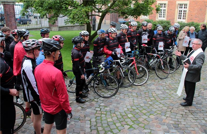 Das Foto zeigt eine Gruppe von Rennradlern, die einen Reisesegen von Weihbischof Geerlings empfangen.