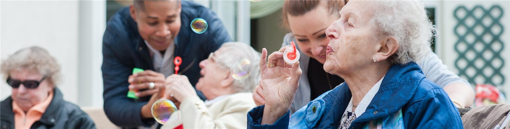 Gäste der Tagspflege und Altenpfleger produzieren Seifenblasen als Atemübung