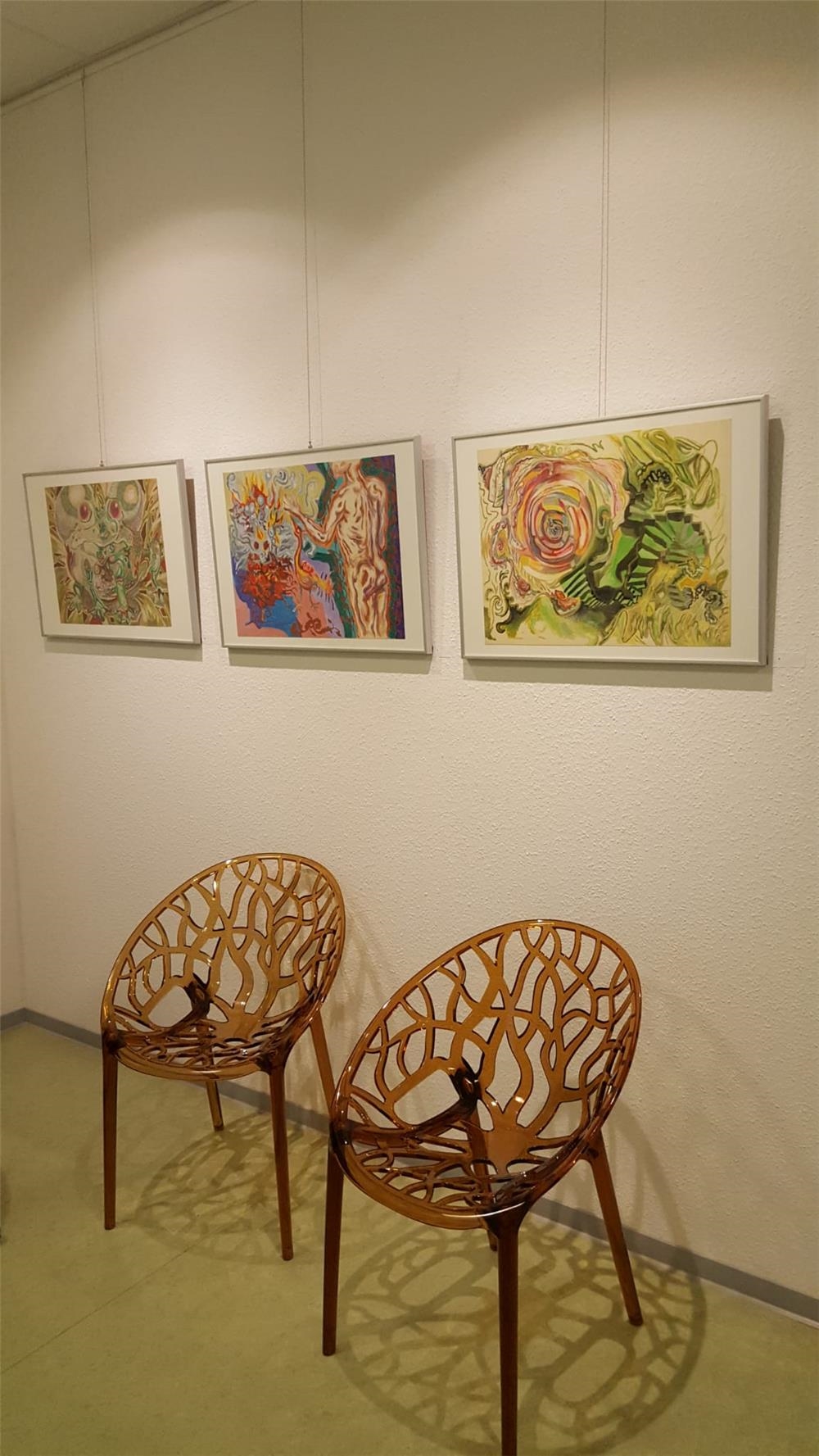 drei bilder der Ausstellung hängen an einer Wand, davor stehen zwei Stühle (© Caritasverband Worms e. V.)