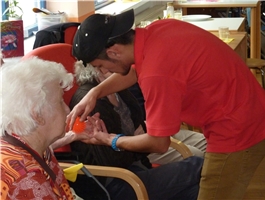 Junger Mann steht vor einer älteren Dame und gibt ihr einen Massageball in die Hand / Foto: Schedlbauer