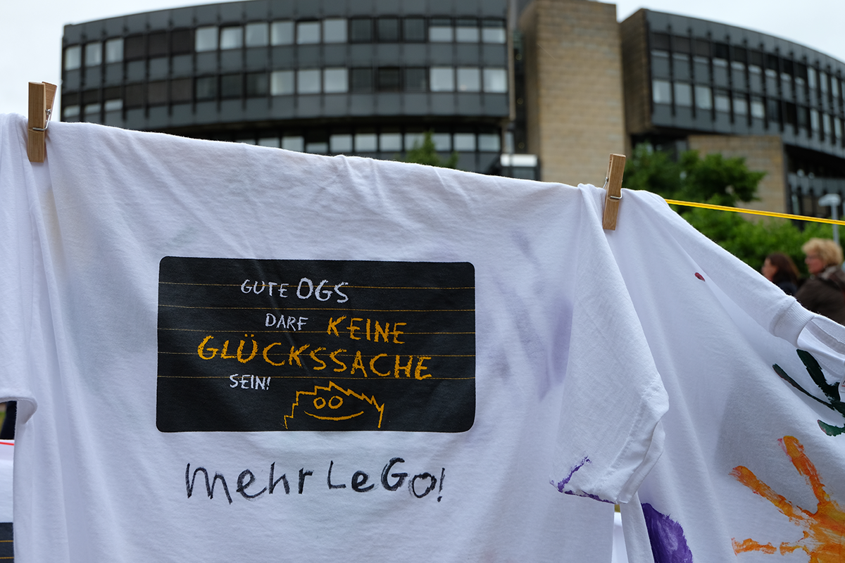 Ein weißes T-Shirt mit dem Logo der OGS-Kampagne der LAG FW NRW und dem Zusatz 'mehr LeGo', dass an einer Wäscheleine vor dem Landtag in Düsseldorf hängt (Markus Lahrmann)