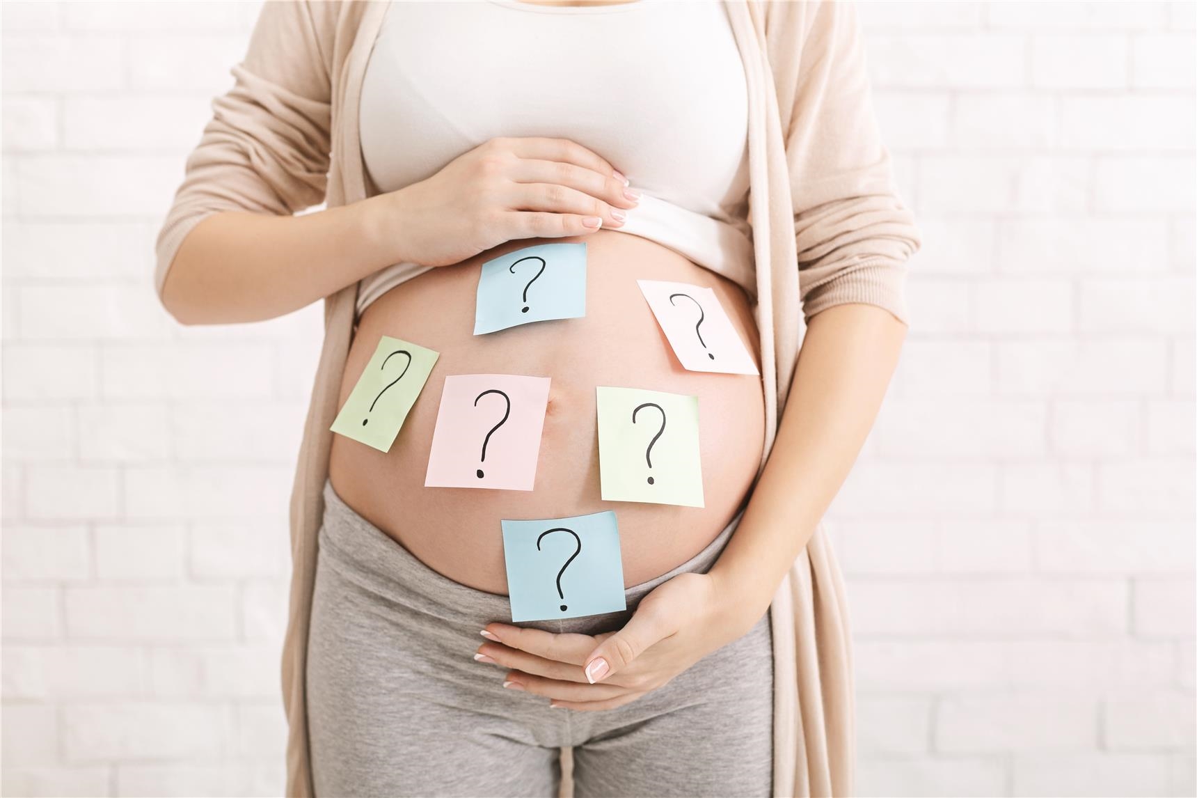 Schwangere Frau mit Post-It-Notes mit Fragezeichen auf dem Bauch (AdobeStock_294069800)