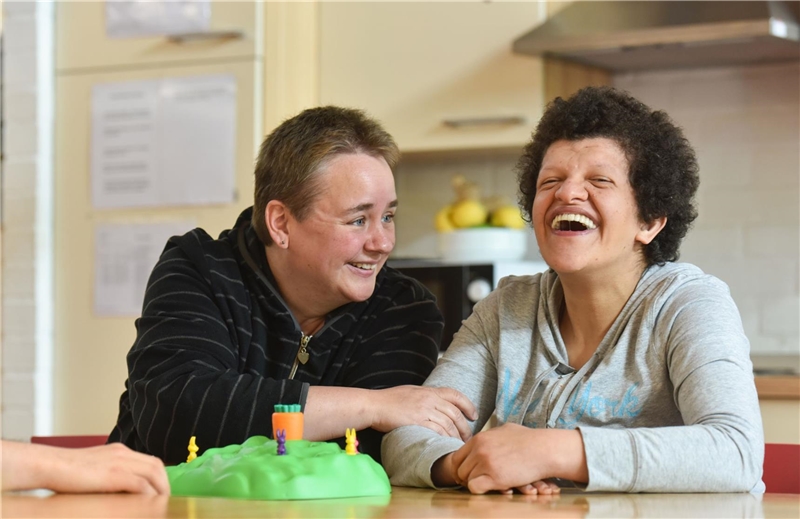 Frau mit Behinderung und Betreuerin lachen und spielen miteinander