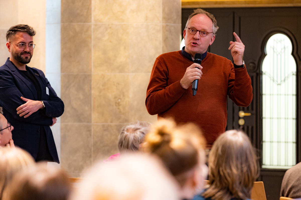 Dr. Uri Kaufmann steht bei der der CiNW-Fachtagung 'Miteinander Gegeneinander?' in der Alten Synagoge in Essen mit einem Mikrofon im Publikum und beteiligt sich an der Podiumsdiskussion (Foto: © Angelika Kamlage | Caritas in NRW)