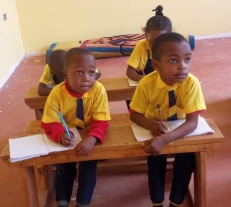 zwei Jungen in gelben Hemden sitzen auf einer Schulbank und schreiben