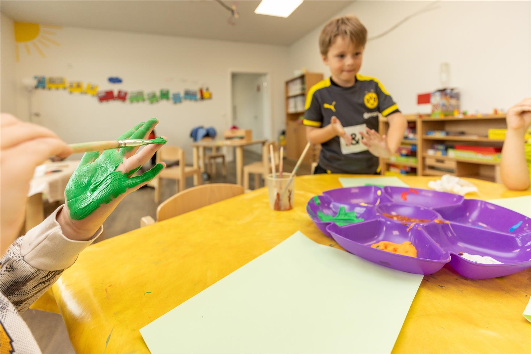 Kinder malen an einem kleinen Tisch mit Fingermalfarbe 