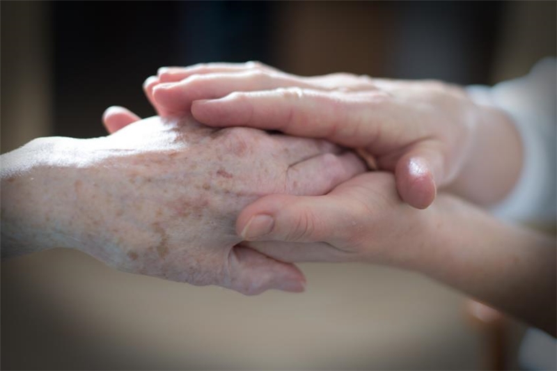 Die Hände eines Senioren werden von jungen Händen gehalten.
