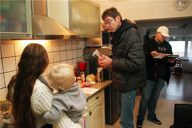 Das Foto zeigt zwei Männer, die in einer Küche mit einer Frau sprechen.