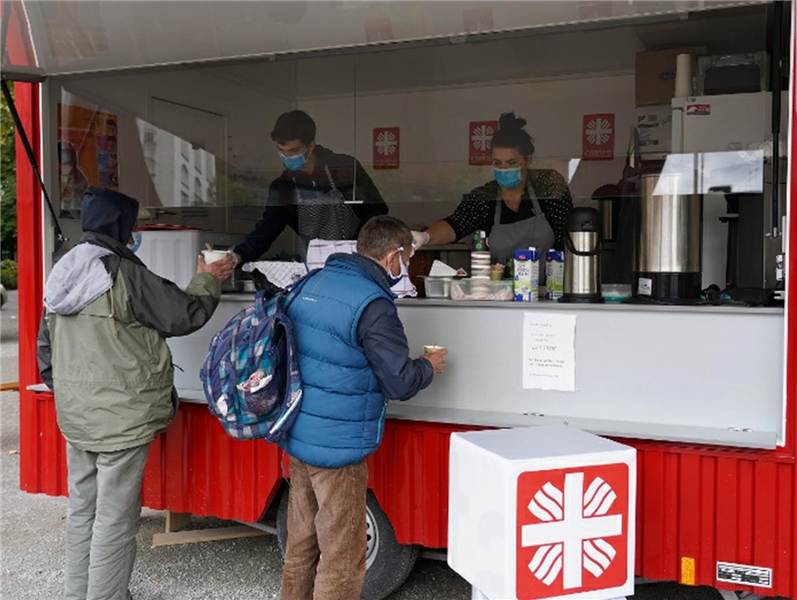 Zwei Männer stehen vor einem Food-Truck, indem drei Personen Essen ausgeben.