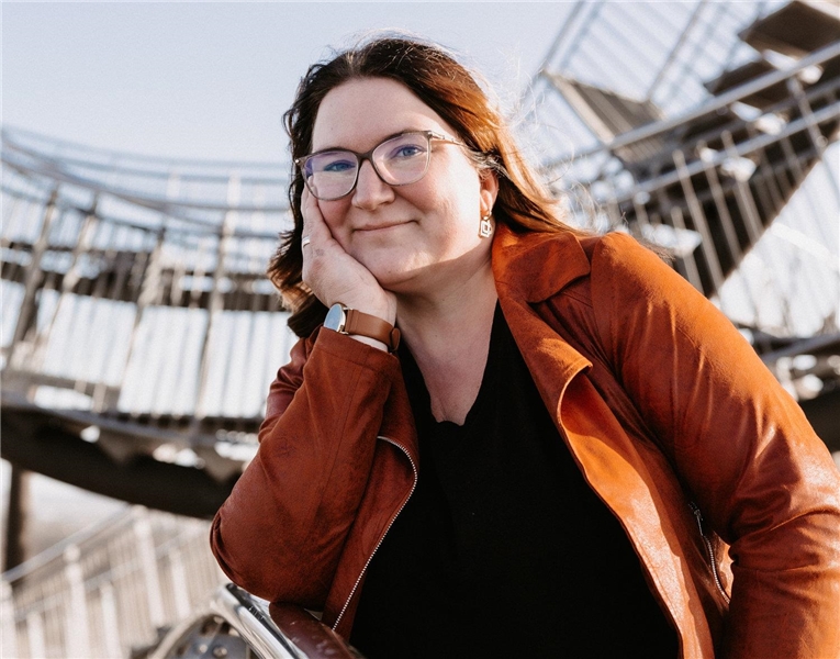 Porträt-Foto einer Frau, die sich auf einem Brückengeländer mit dem Ellbogen abstützt und ihr Kinn in der Hand hält.