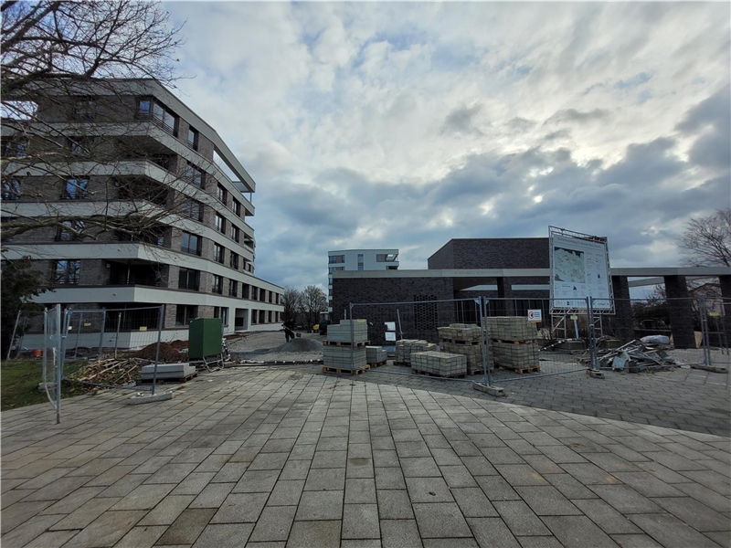 Ein Blick auf das Neubauprojekt Mönchfeld: Über einen gepflasterten Platz sieht man ein Wohngebäude und das neue Kirchengebäude