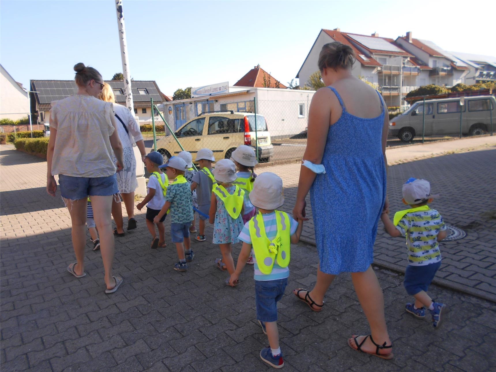 eine Kindergruppe mit gelben Warnwesten wird von Erzieherinnen auf dem Weg zum Spielplatz begleitet