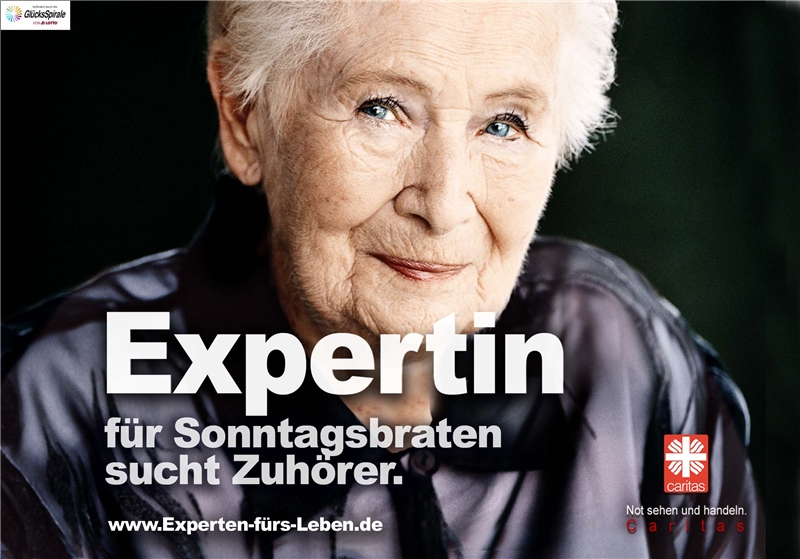 Ältere Frau schaut freundlich, auf dem Plakat steht "Expertin für Sonntagsbraten sucht Zuhörer".
