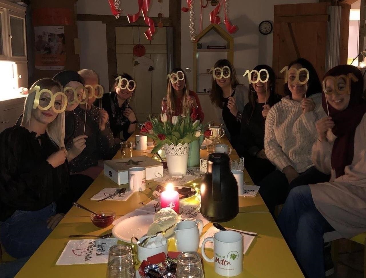 Neun Frauen sitzen um einen Tisch und halten sich eine "100"-Brille vor das Gesicht (Kita St. Laurentius)
