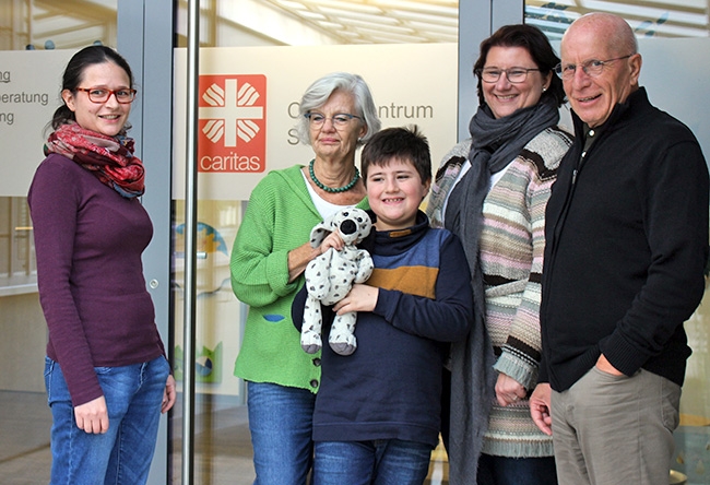 Gruppenbild: Ein Kind mit Stofftier, drei Frauen und ein Mann vor Gebäude mit Caritas-Logo (Caritasverband Darmstadt e. V.)