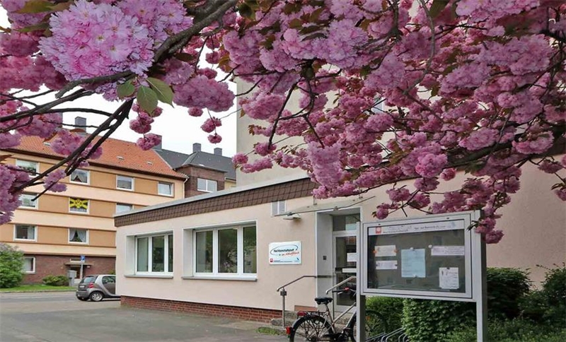 Blick auf den Eingang des Nachbarschfaftstreffs mit einem blühenden Kirschbaum im Vordergrund