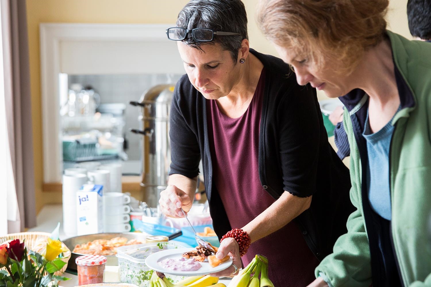 Zwei Frauen stehen am Frühstücksbuffet und füllen ihre Teller (Deutscher Caritasverband e. V. / Sebastian Pfütze)