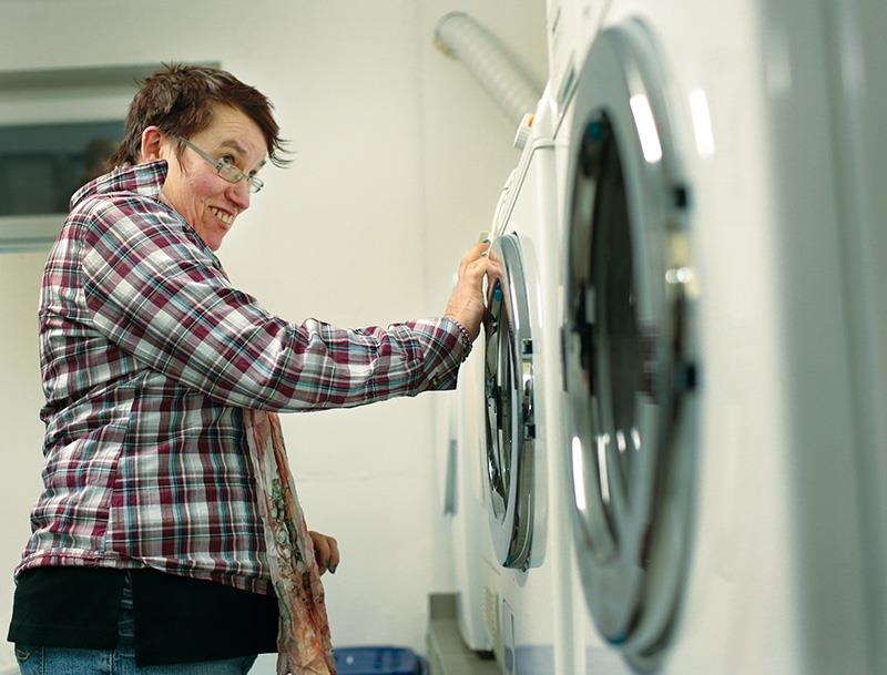 Frau mit Behinderung drückt Taste an Waschmaschine (Thilo Schmülgen, Aktion Mensch)