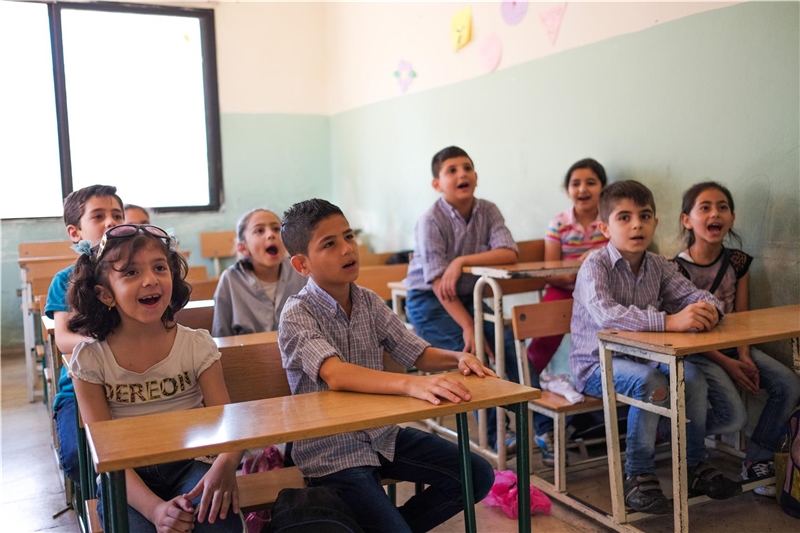 Mehrere Kinder sitzen jeweils zu zweit an einem Tisch in der Schule.