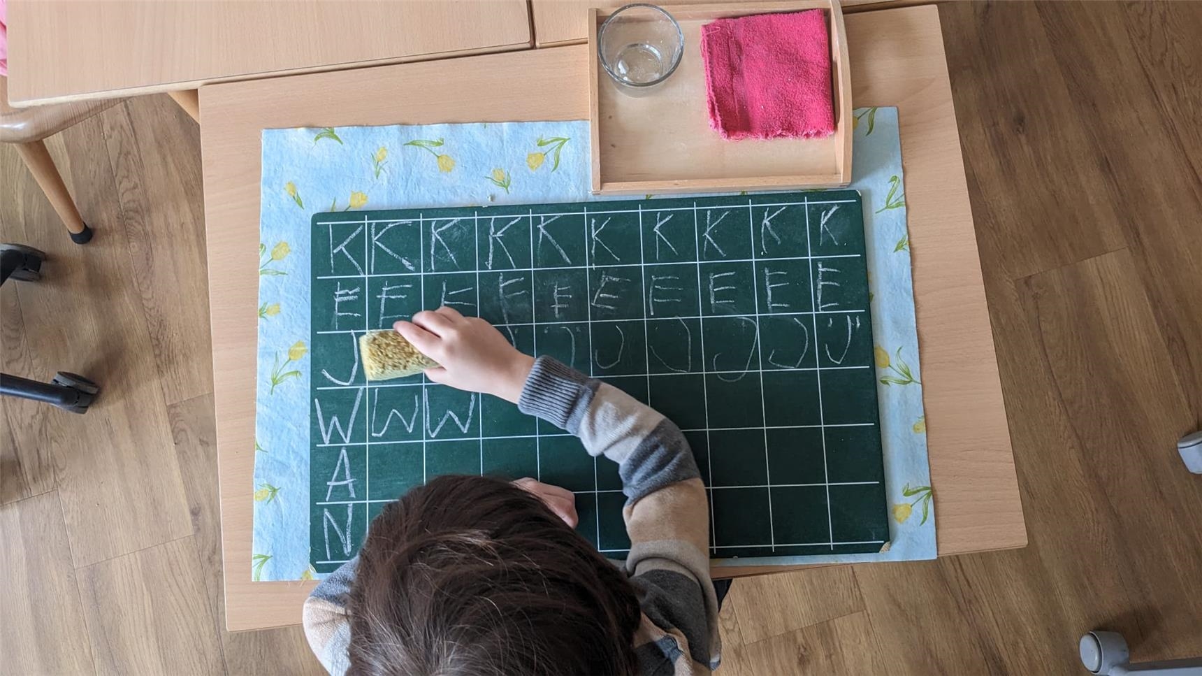 Ein Mädchen schreibt einzelne Buchstaben auf eine Tafel 