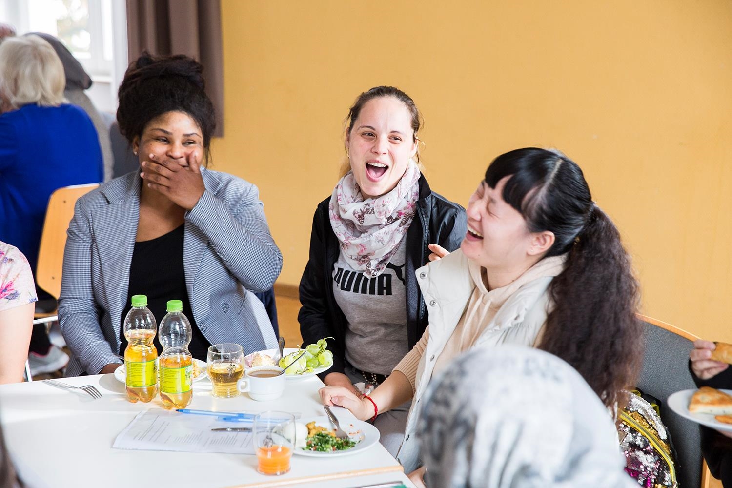 Drei jungen Frauen sitzen am Essenstisch und lachen lauthals (Deutscher Caritasverband e. V. / Sebastian Pfütze)