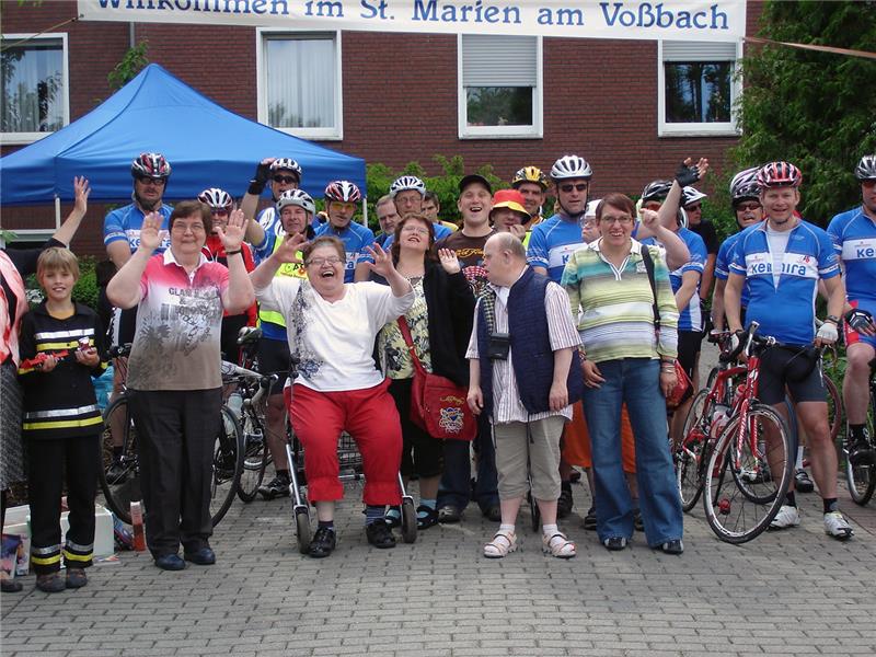 Das Foto zeigt eine Gruppe von Menschen vor einem Banner, zum einen Bewohner eines Behindertenwohnheims und dazu Rennradfahrer in Montur.