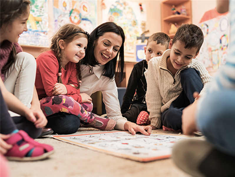 Eine Erzieherin zeigt Kindern, die viel Spaß haben, etwas auf dem Boden