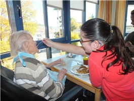 Eine junge Frau sitzt vor einer Seniorin und reicht ihr mit einem Löffel das Essen an / Foto: Schedlbauer