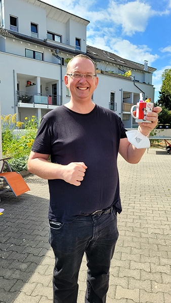 Ein Mann hält mit Freude eine Tasse mit Caritas Jubiläums-Aufdruck in der Hand (Caritasverband Darmstadt e. V.)
