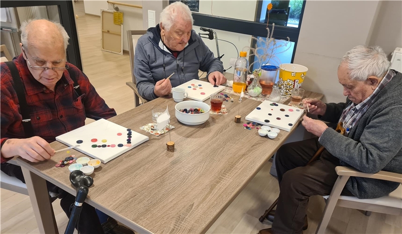 Drei Senioren sitzen an einem Tisch und basteln mit Köpfen Bilder