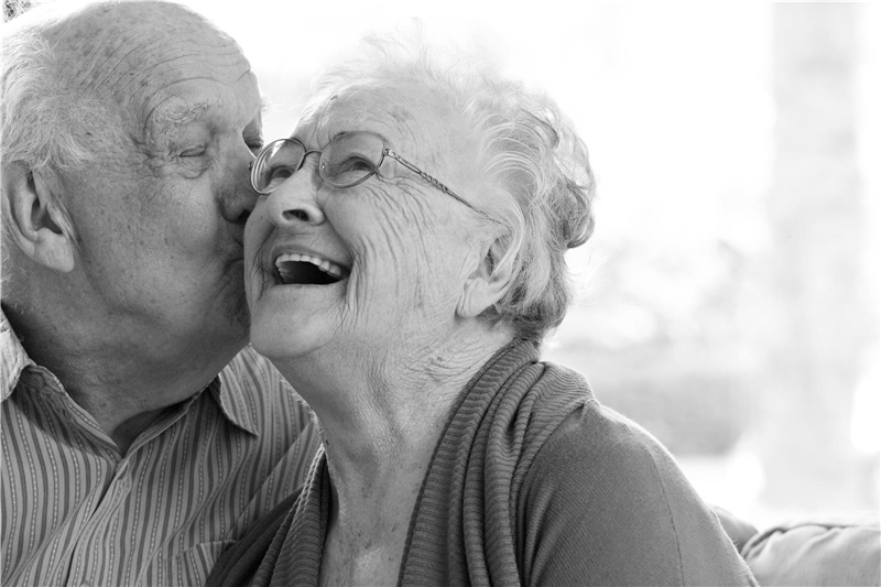Ein älterer Herr küsst eine fröhlich wirkende ältere Frau