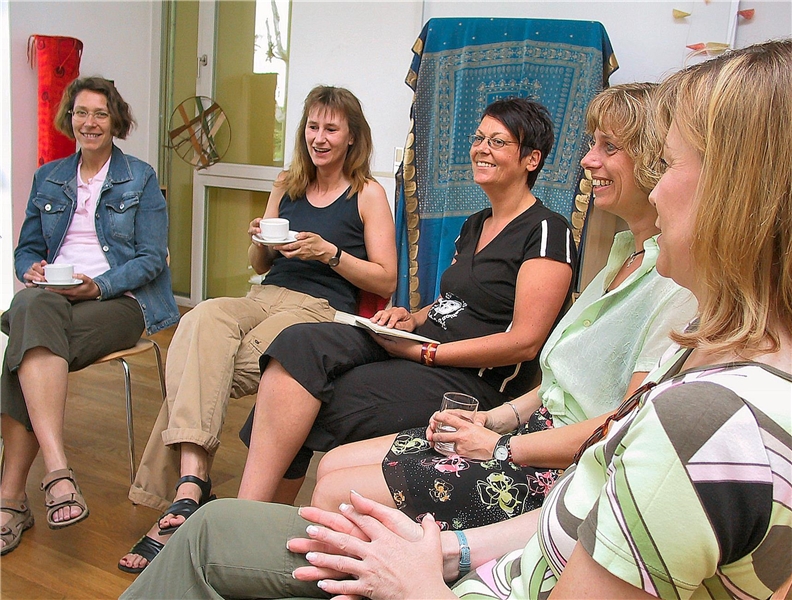 Das Foto zeigt eine Gruppe Frauen, die im Kreis sitzen und Spaß miteinander haben.