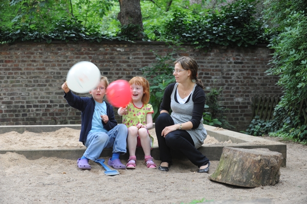 zwei Kinder mit einer Frau im Sand und einem Luftballon
