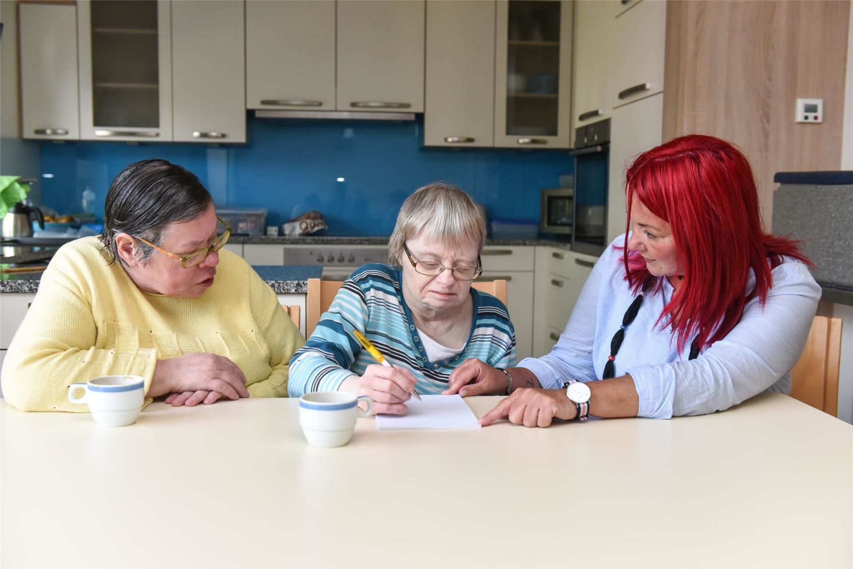 Sozialarbeiterin unterstützt zwei Frauen beim Schreiben (Foto : Deutscher Caritasverband / Harald Oppitz)