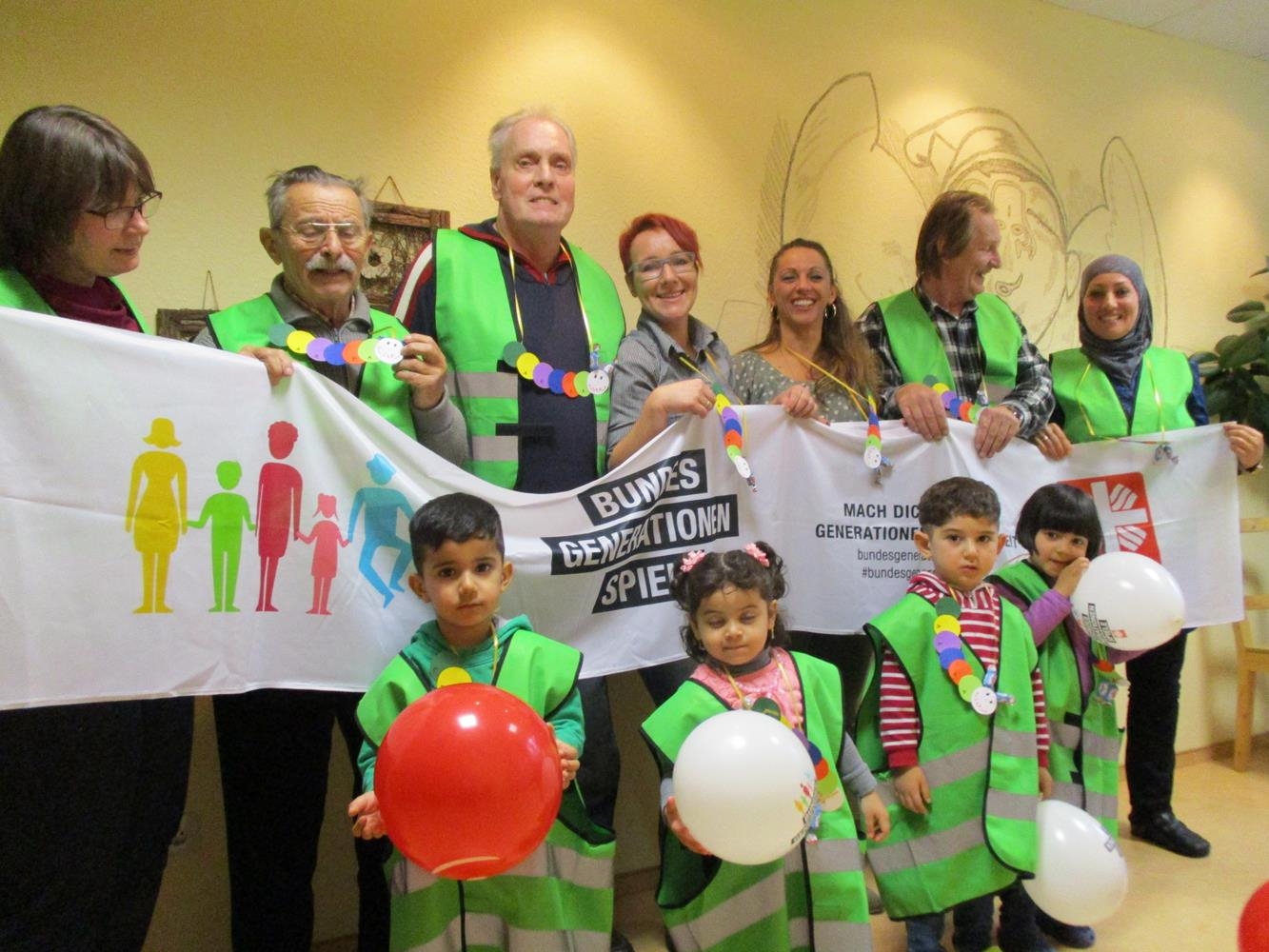 Gruppenfoto mit Erwachsenen und kleinen Kindern in grünen Westen und mit Banner. (Caritas Tagespflege Heilig Geist)