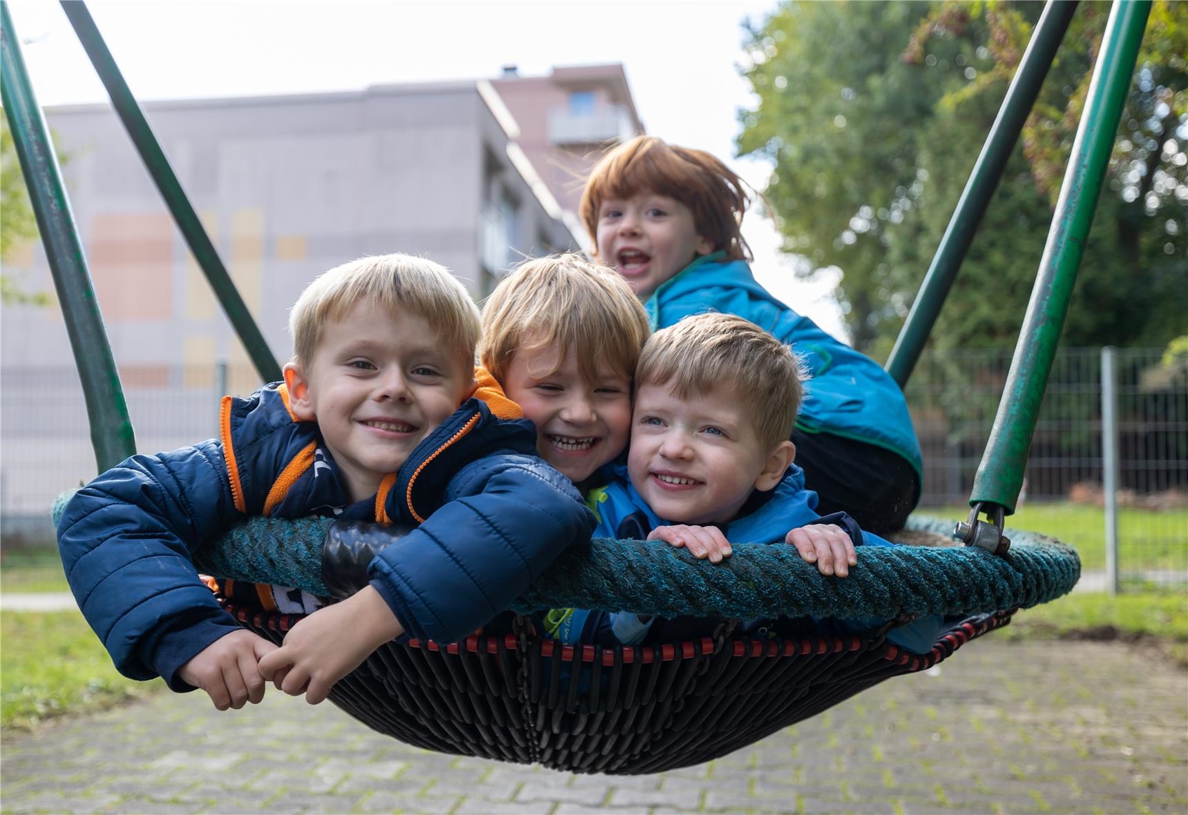 Vier Jungen sitzen lachend in einer Nestschaukel. 