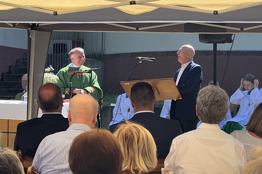 Ein Mann an einem Rednerpult hält einem Pfarrer eine Ansprache (Caritasverband Darmstadt e. V. / Jens Berger)
