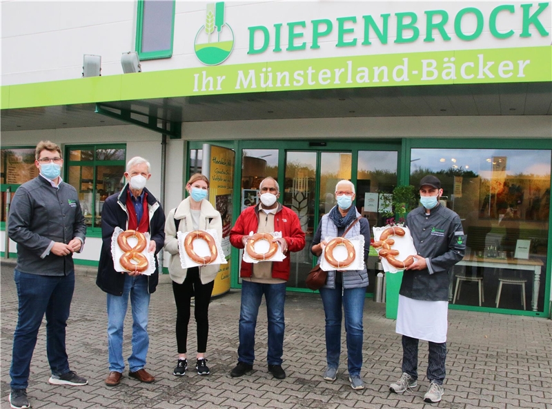 Das Foto zeigt eine Gruppen von Menschen, die aufgereiht vor einer Bäckerei eine 8000 aus Laugengebäck geformt in die Kamera zeigen.