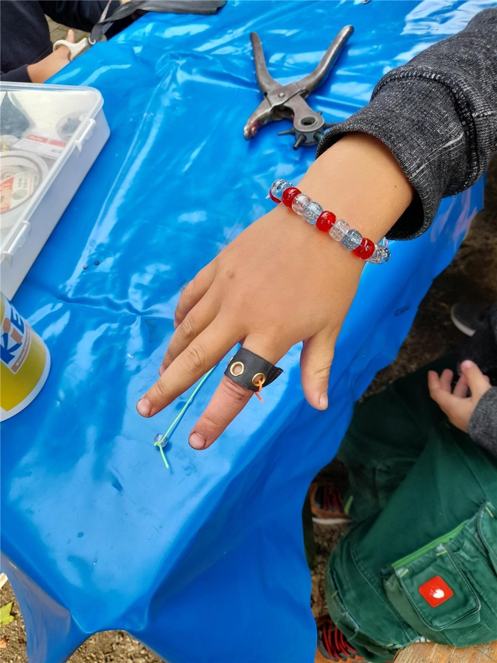 Kinderhand. Auf dem Zeigefinger steckt ein Ring aus Fahrradschlauch mit mehreren Ösen und einem orangenen Band, das durch zwei Ösen gezogen ist. (Christina Wunderlich)