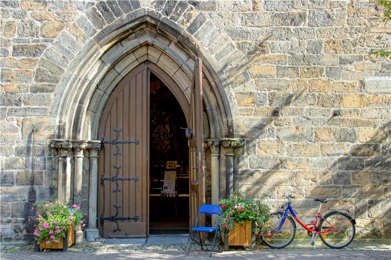 Offene Holztür einer Kirche in Norddeutschland. Blauer Klappstuhl am Eingang und Fahrrad an der Wand.