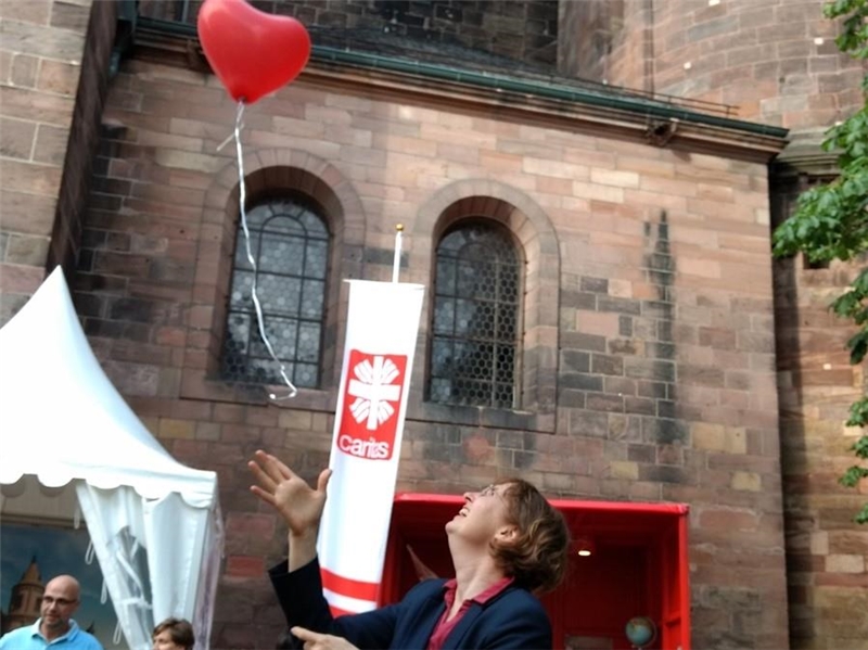 Frau lässt vor Kirche einen roten Luftballon fliegen.