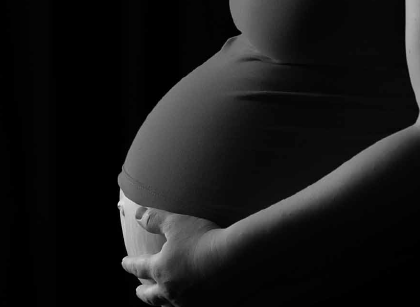 Eine Frau, die Ihre linke Hand auf ihren Schwangerschaftsbauch legt. Die Aufnahme ist in schwarz-weiß.