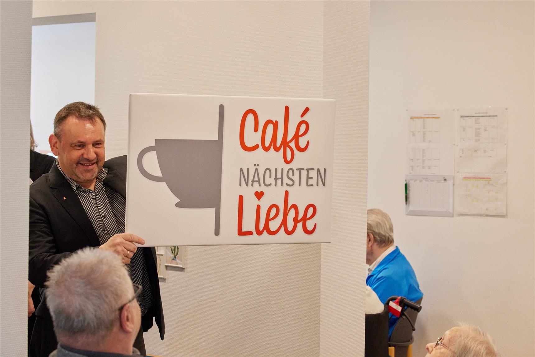 Rainer Lehmler präsentiert das Schild Café Nächstenliebe. (Caritasverband Westerwald-Rhein-Lahn e.V. / Olaf Nitz)