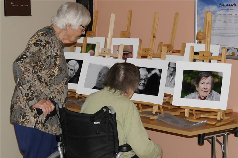 Foto von zwei Seniorinnen, die im Eingangsbereich des Altenzentrums die ausgestellten Porträtaufnahmen betrachten