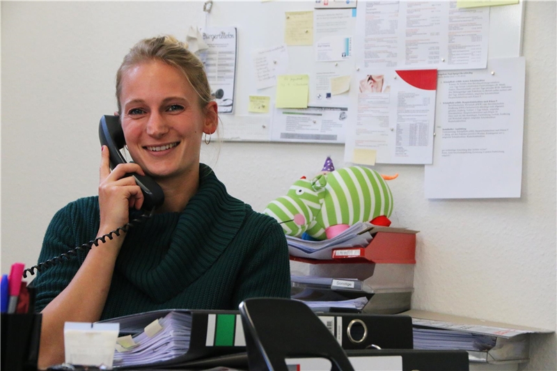 Das Foto zeigt eine junge Frau, die an einem Schreibtisch telefoniert.