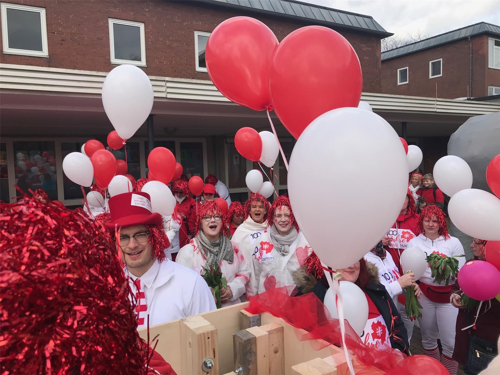 Rot-weiß gekleidete Frauen mit roten Perücken, Luftballons und Tulpen (Caritas Hamm)