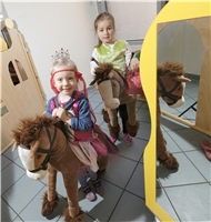 Zwei kleine Mädchen haben sich als Burgfräuleins verkleidet und reiten auf einem Stoffpferd / D. Wäsche