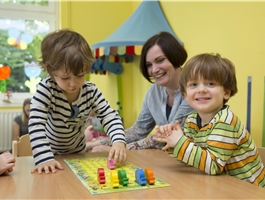 Eine Erzieherin spielt mit zwei Kindern ein Brettspiel / Dietmar Wäsche